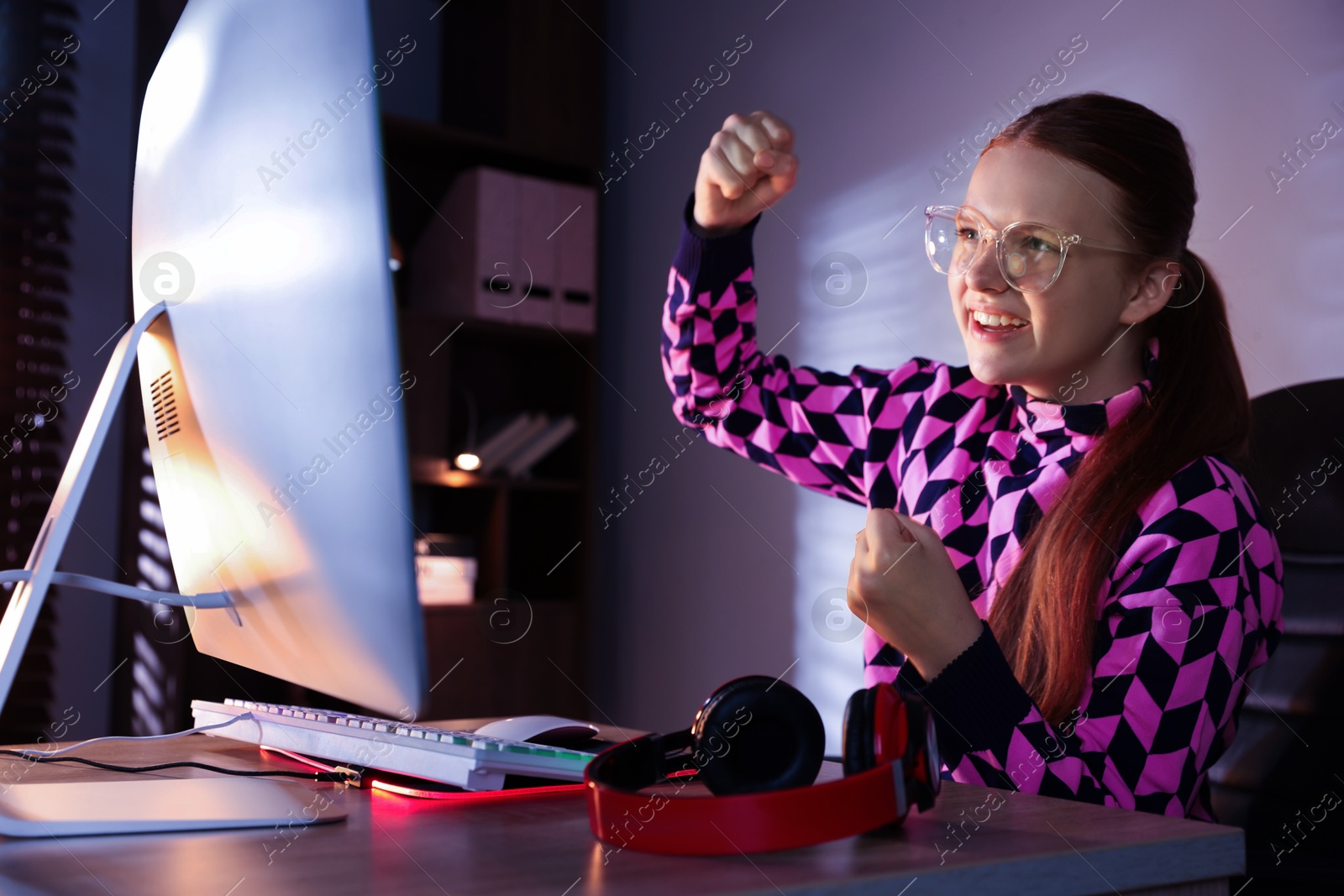 Photo of Happy girl playing video game with keyboard at table indoors