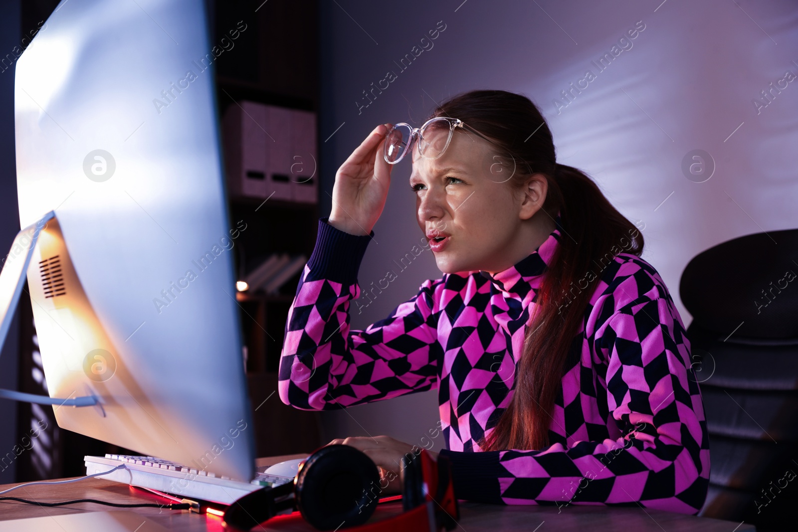 Photo of Girl looking at monitor at table with keyboard and headphones indoors