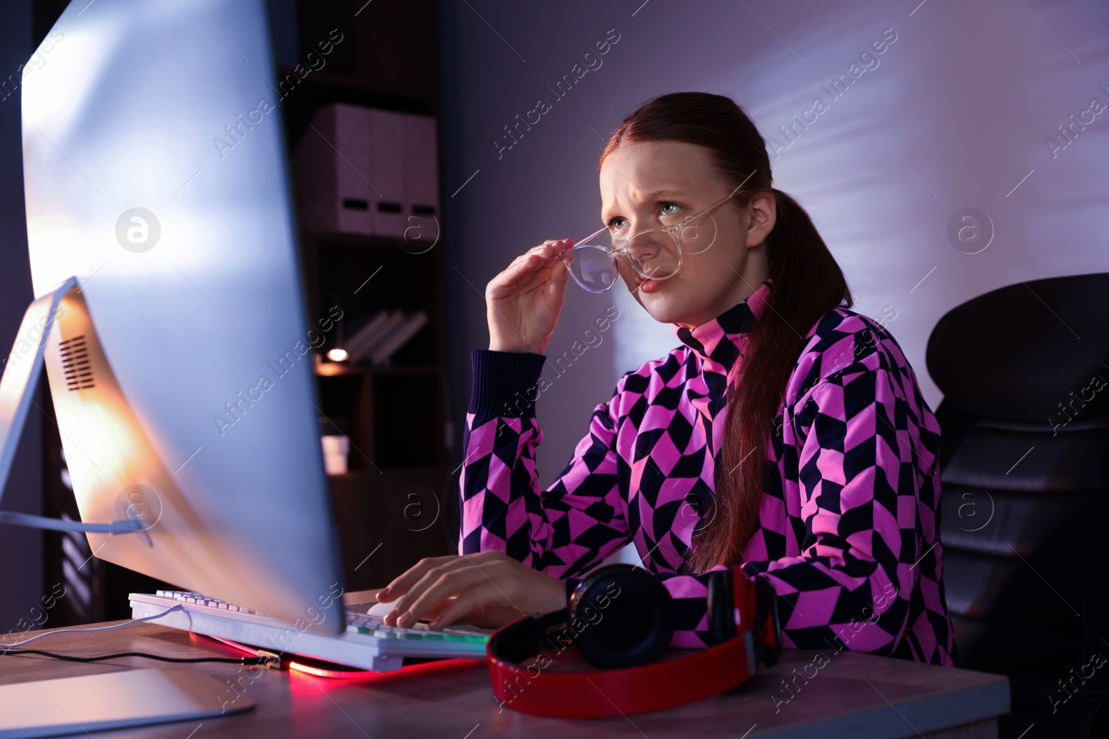 Photo of Girl looking at monitor at table with keyboard and headphones indoors