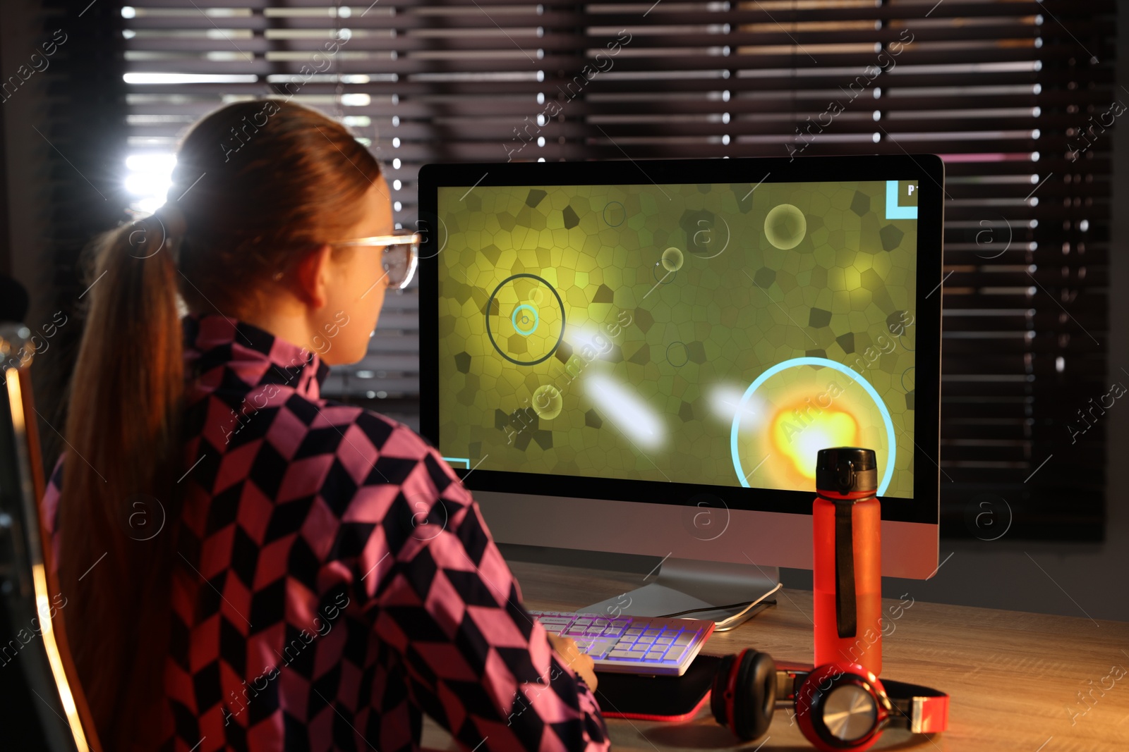 Photo of Girl playing video game with keyboard at table indoors, back view