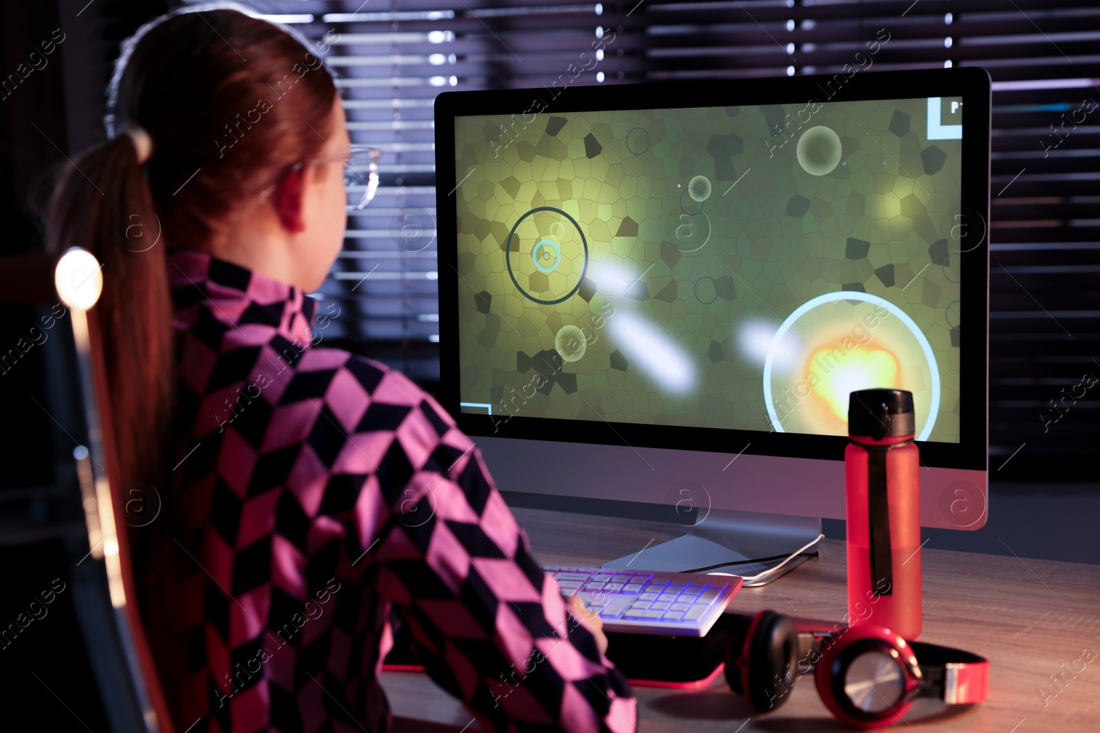 Photo of Girl playing video game with keyboard at table indoors, back view