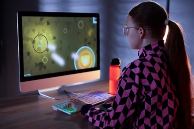 Girl playing video game with keyboard at table indoors, back view