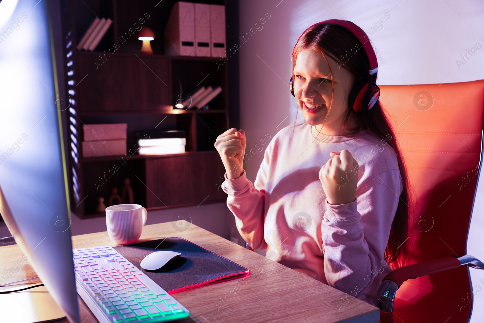 Photo of Happy girl playing video game with keyboard and mouse at table indoors