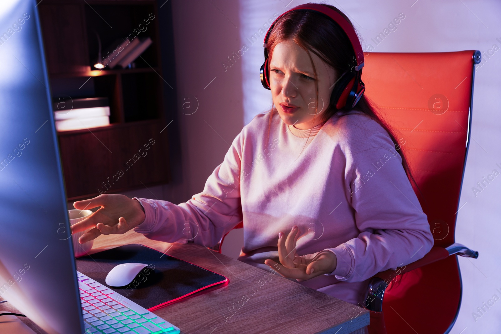 Photo of Emotional girl playing video game with keyboard and mouse at table indoors