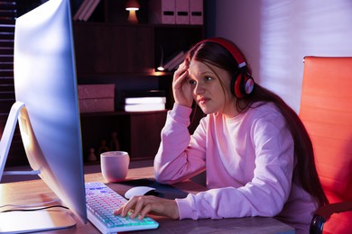 Emotional girl playing video game with keyboard and mouse at table indoors