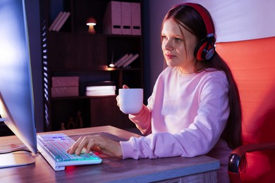 Girl in headphones with coffee cup using computer keyboard at table indoors