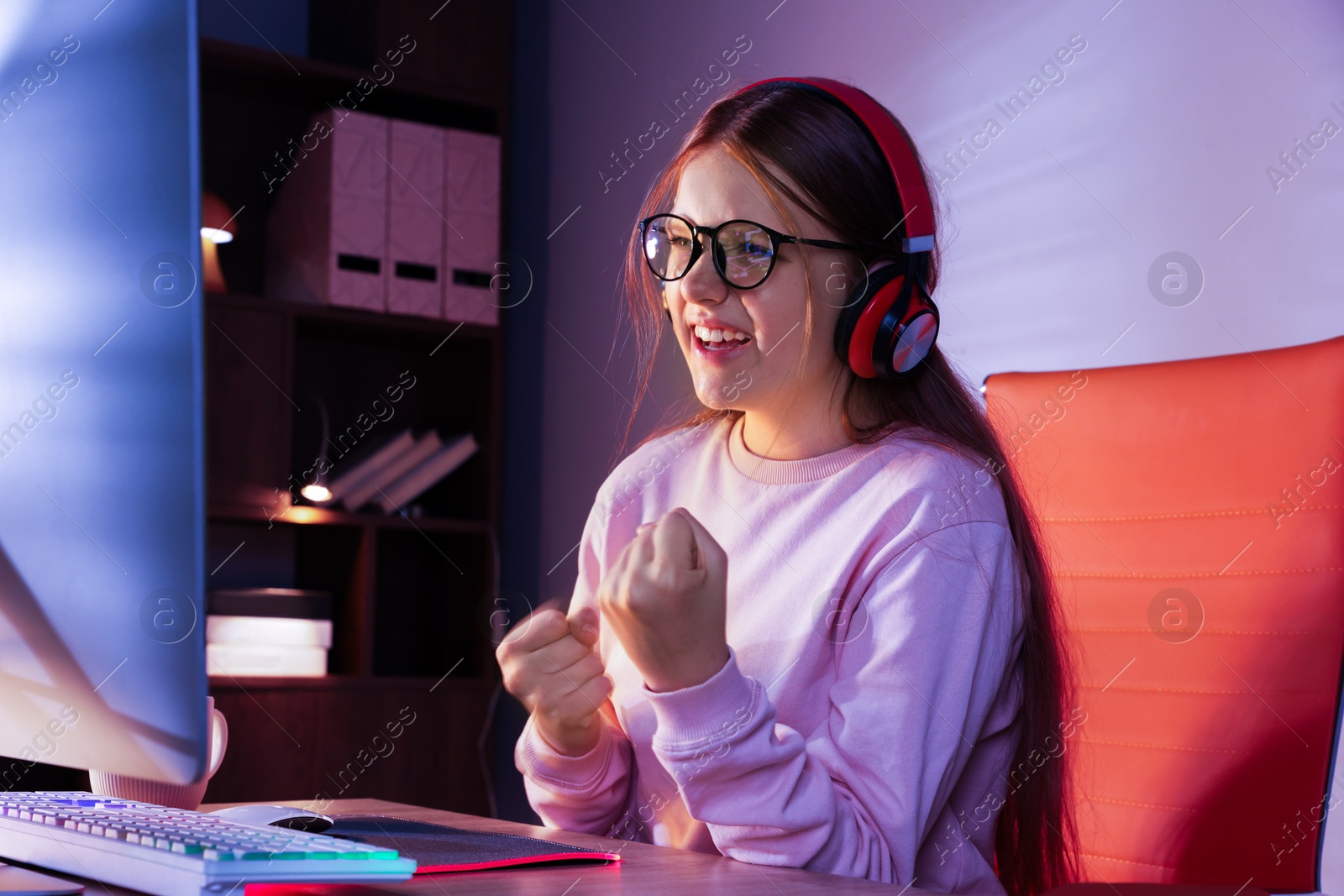 Photo of Happy girl playing video game with keyboard at table indoors