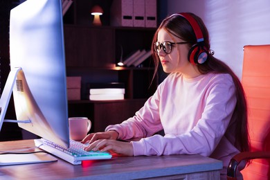 Photo of Girl in headphones using computer keyboard at table indoors