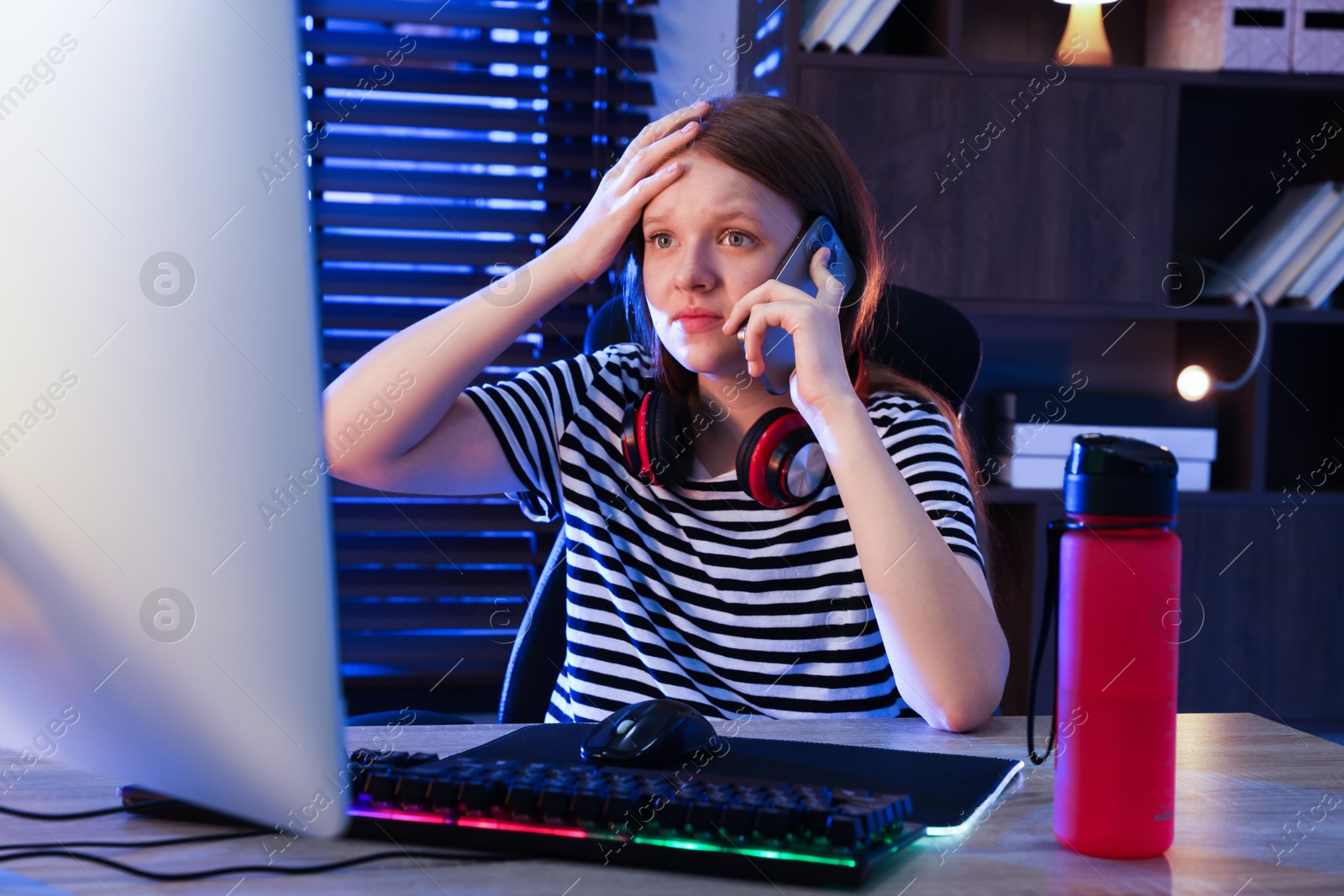 Photo of Emotional girl talking by smartphone at table with keyboard and mouse indoors