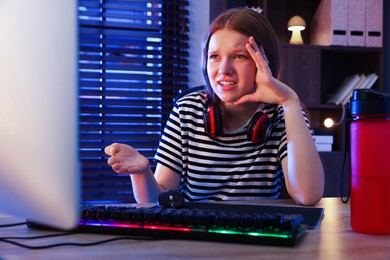 Emotional girl playing video game with keyboard and mouse at table indoors