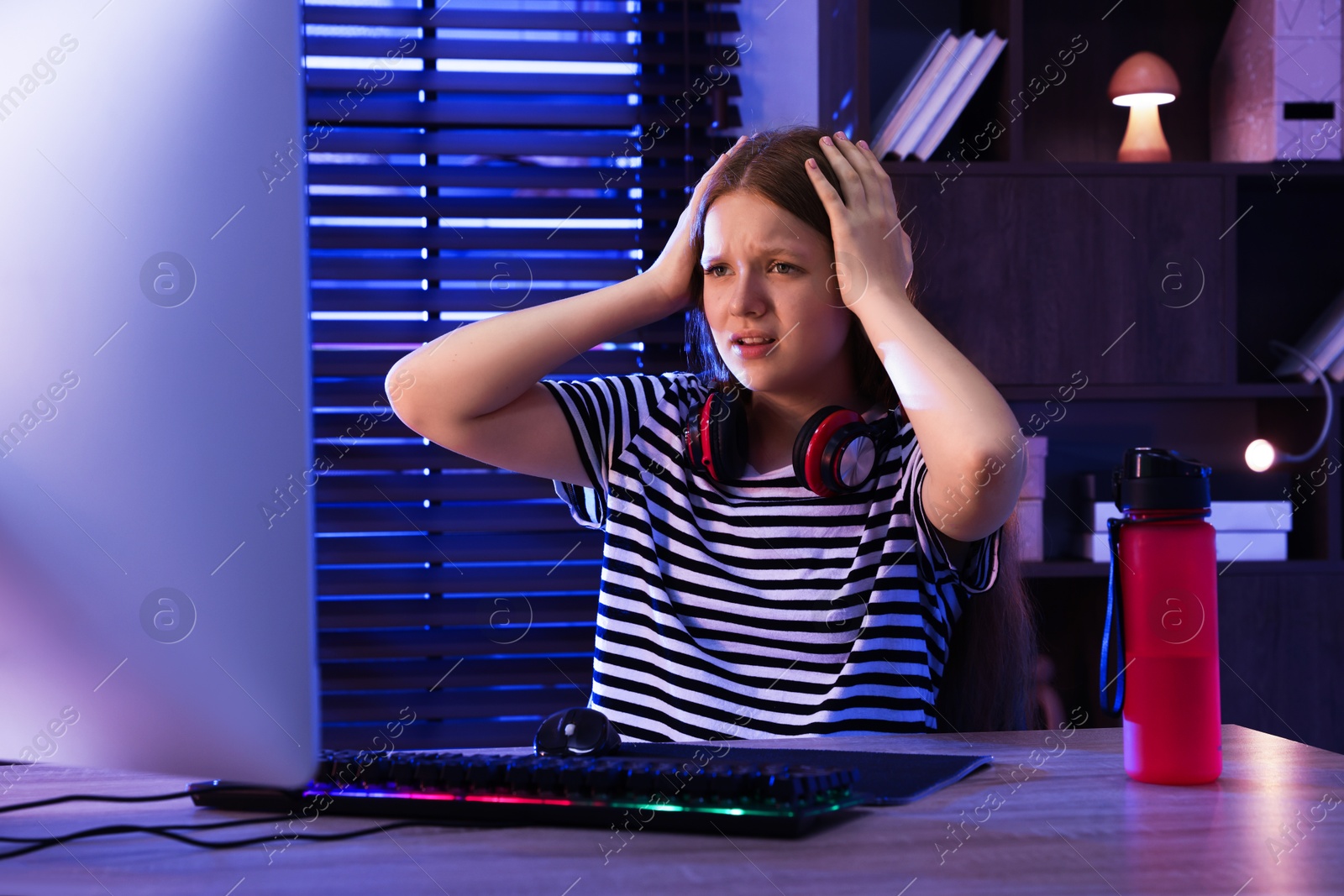 Photo of Emotional girl playing video game with keyboard and mouse at table indoors