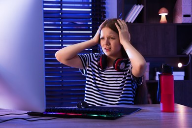 Photo of Emotional girl playing video game with keyboard and mouse at table indoors