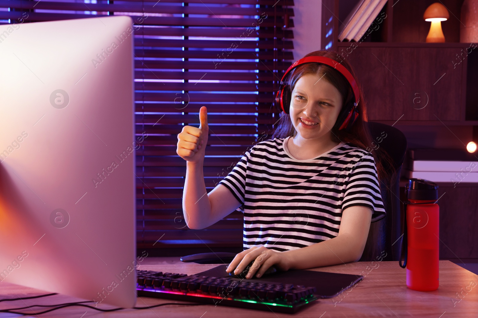 Photo of Happy girl playing video game with keyboard and mouse at table indoors