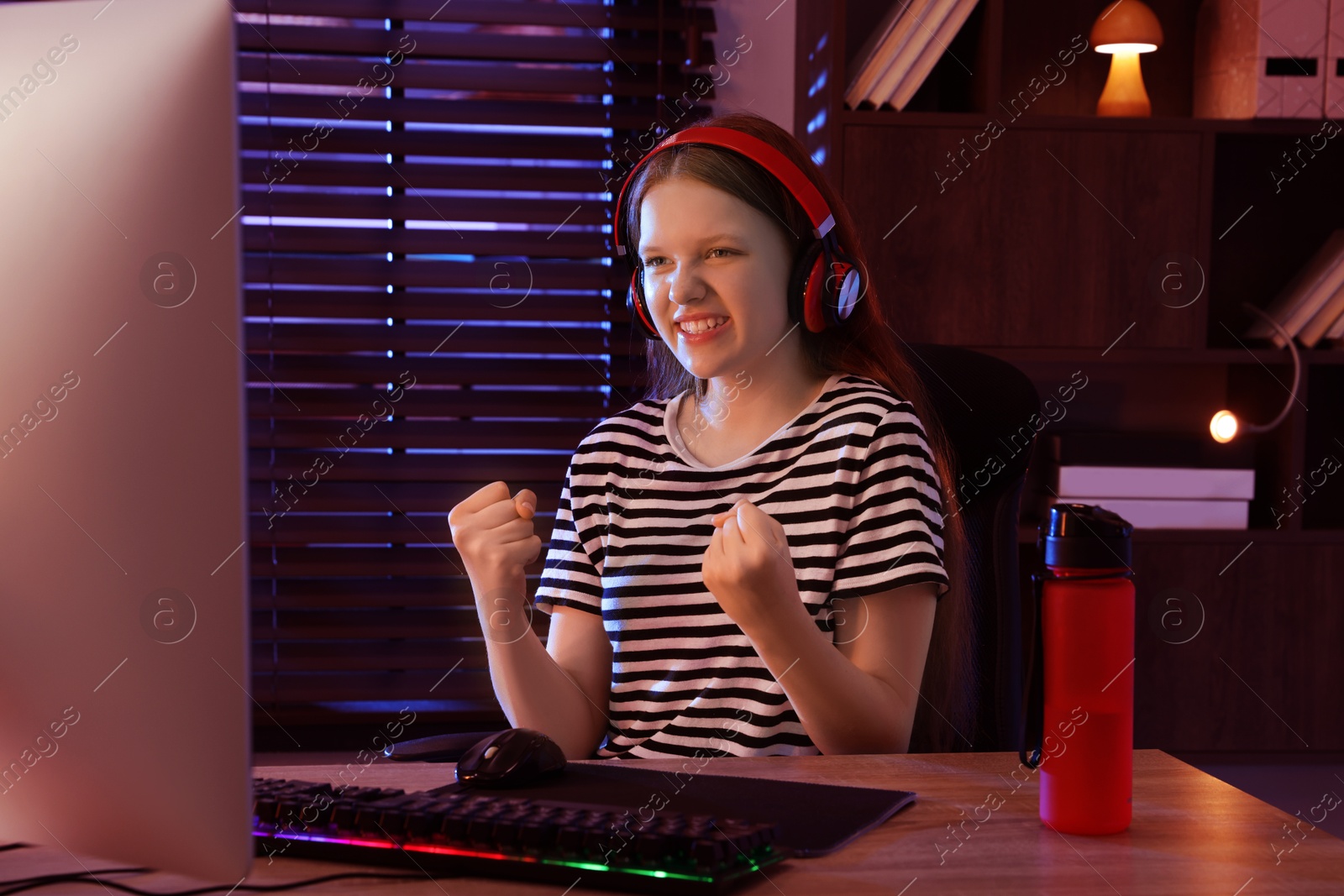 Photo of Happy girl playing video game with keyboard and mouse at table indoors