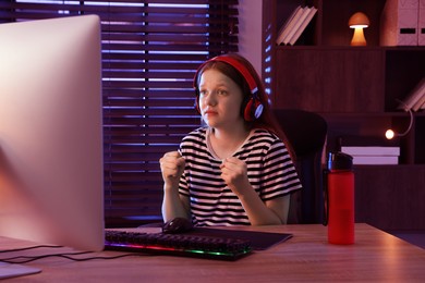 Photo of Emotional girl playing video game with keyboard and mouse at table indoors