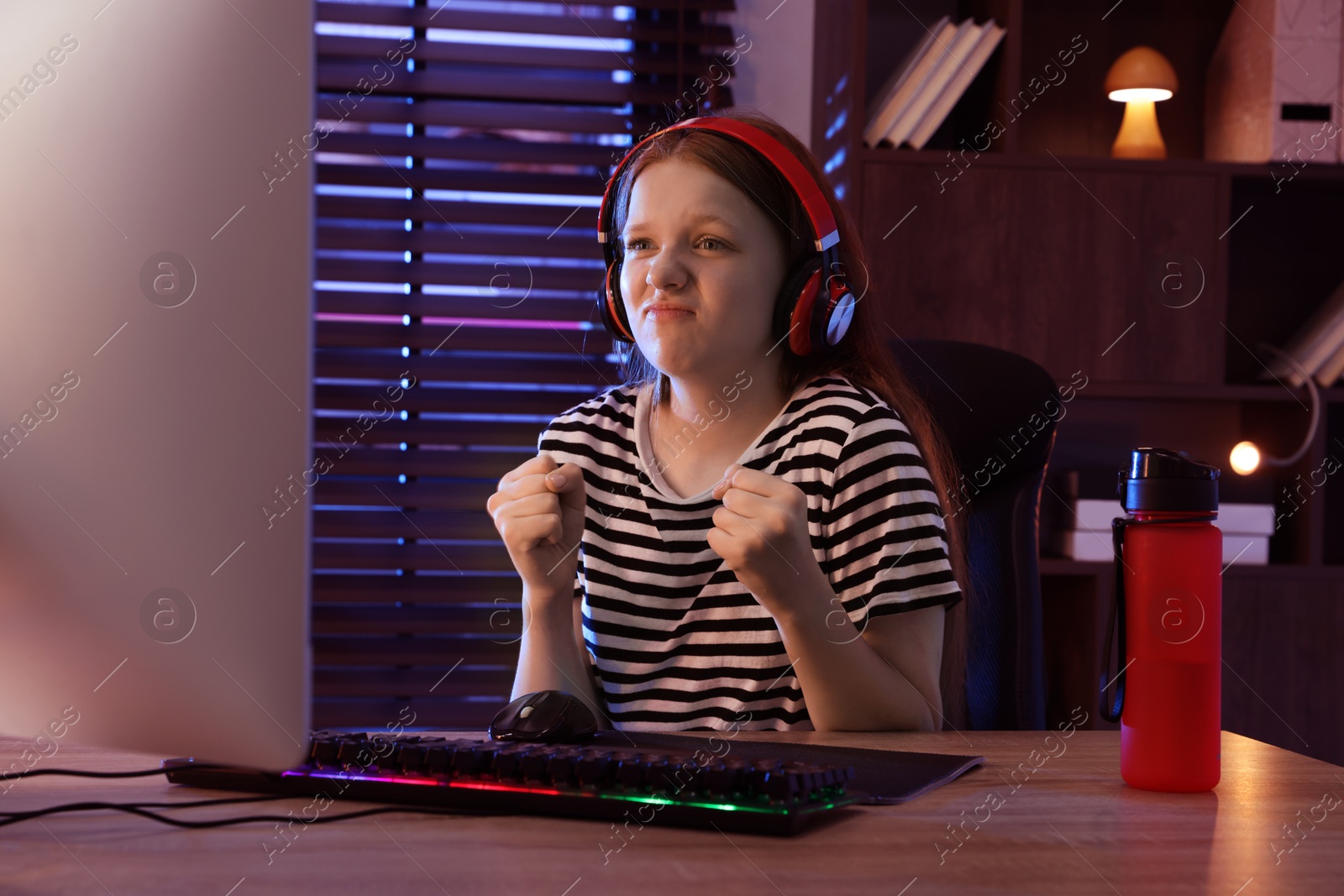 Photo of Emotional girl playing video game with keyboard and mouse at table indoors