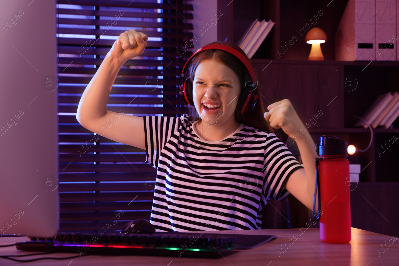 Photo of Happy girl playing video game with keyboard and mouse at table indoors