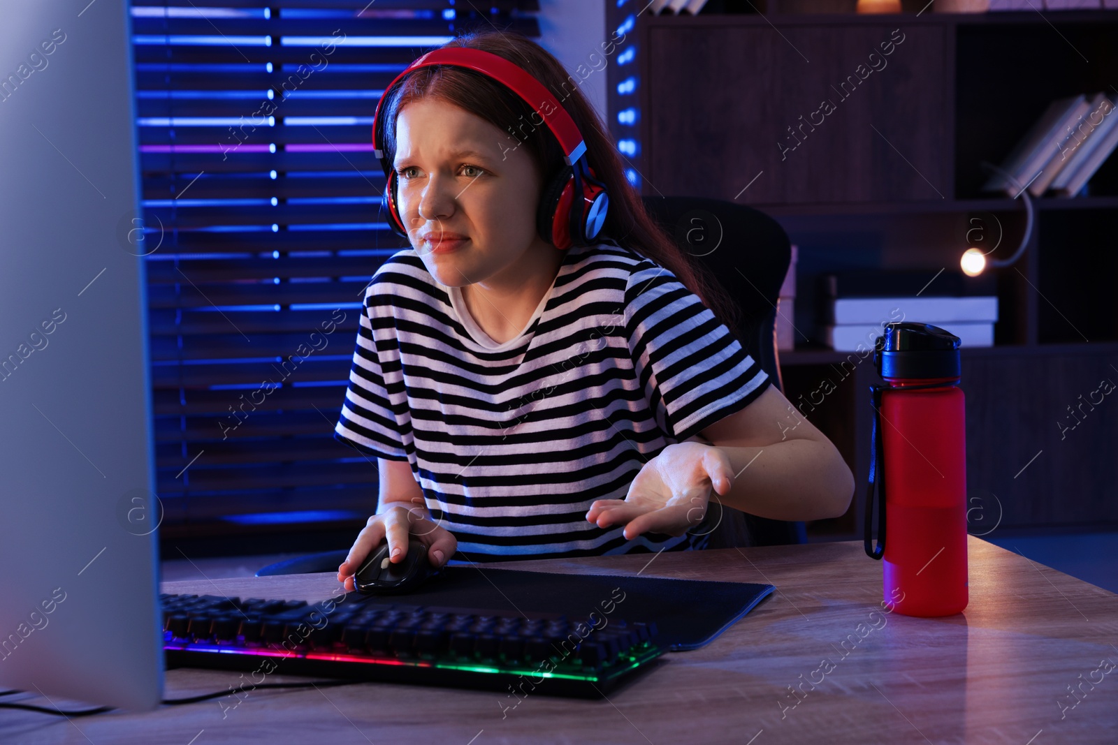 Photo of Emotional girl playing video game with keyboard and mouse at table indoors