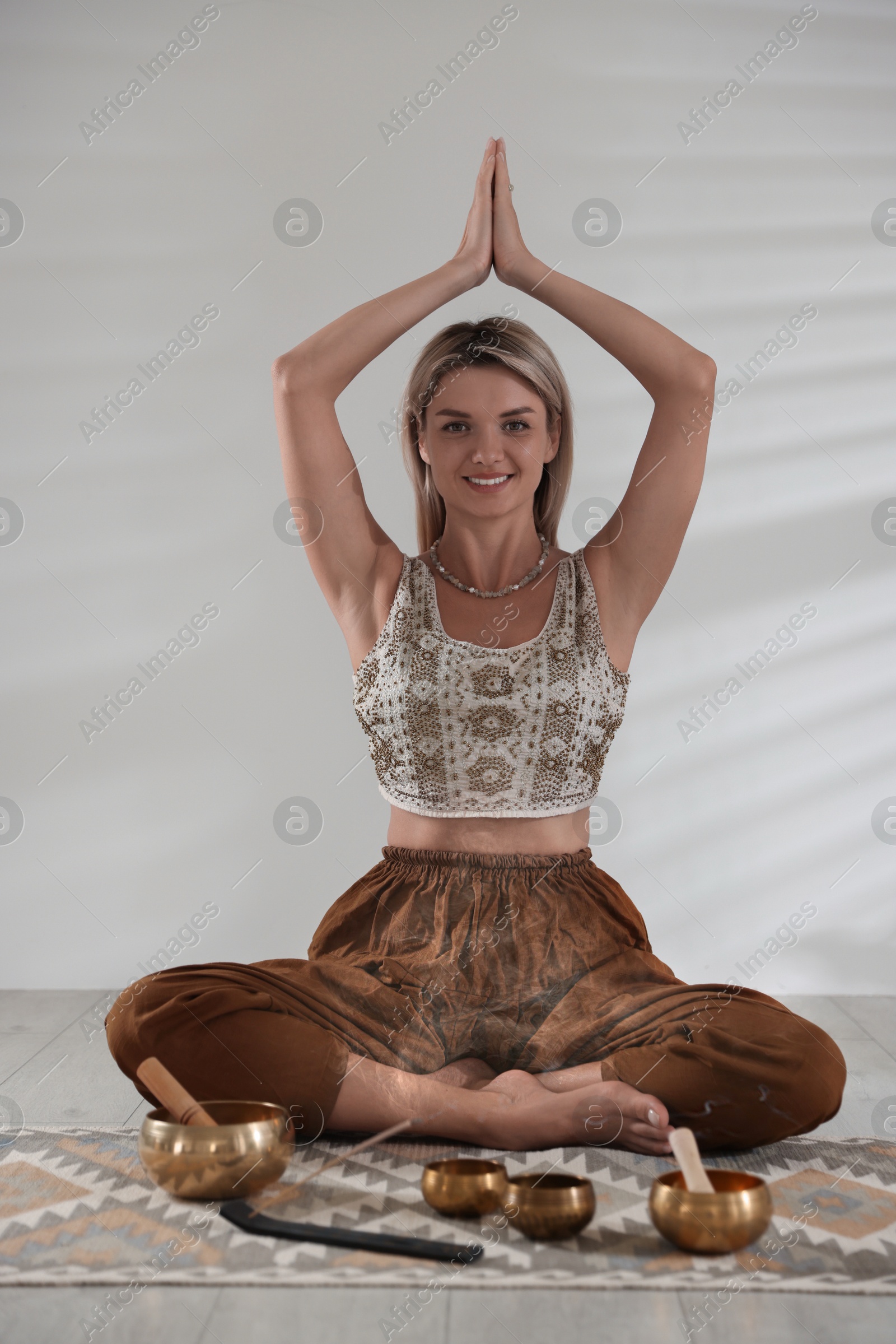 Photo of Beautiful young woman with smoldering incense stick and tibetan singing bowls meditating on floor indoors