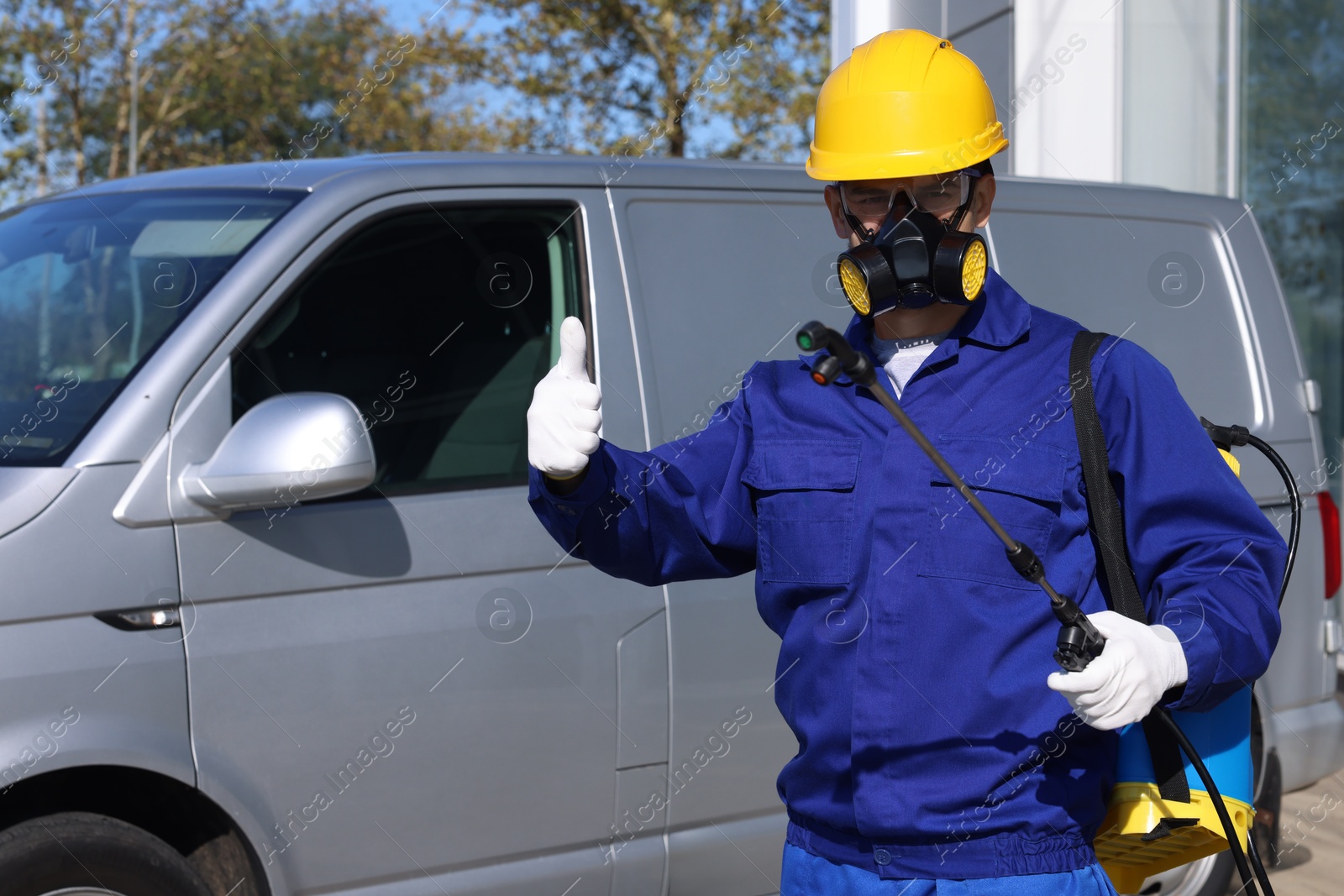 Photo of Pest control worker with spray tank showing thumbs up outdoors