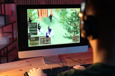 Photo of Young man playing video game with keyboard at wooden table indoors, back view