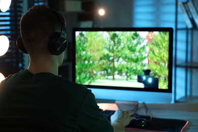 Photo of Young man playing video game with keyboard at wooden table indoors, back view