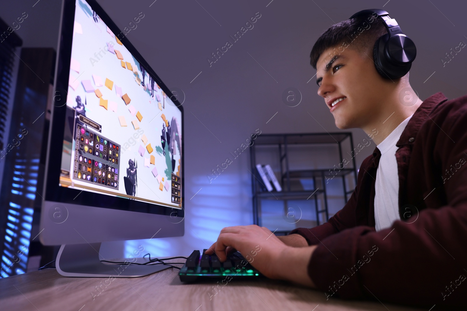 Photo of Young man playing video game with keyboard at wooden table indoors, low angle view