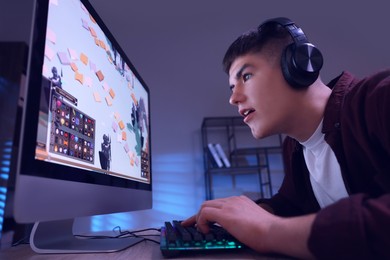 Photo of Young man playing video game with keyboard at wooden table indoors, low angle view