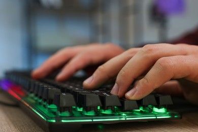 Photo of Young man using computer keyboard at wooden table indoors, closeup