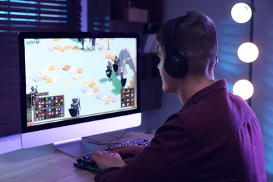 Photo of Young man playing video game at wooden table indoors, back view