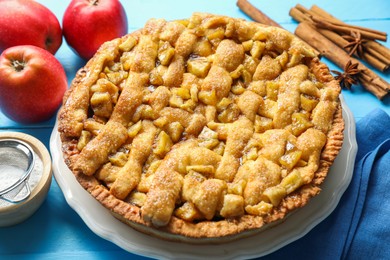 Photo of Homemade apple pie and ingredients on light blue wooden table, closeup