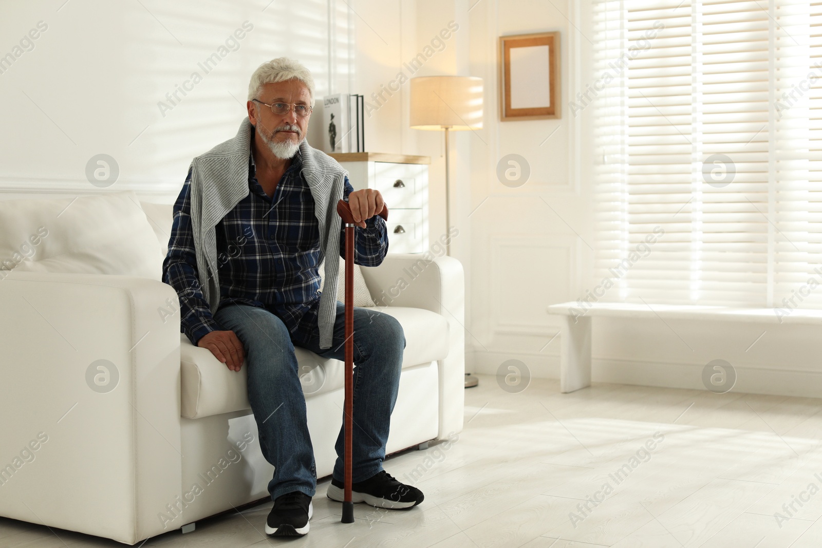 Photo of Lonely senior man with walking cane sitting on sofa at home. Space for text