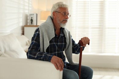 Photo of Lonely senior man with walking cane sitting on sofa at home