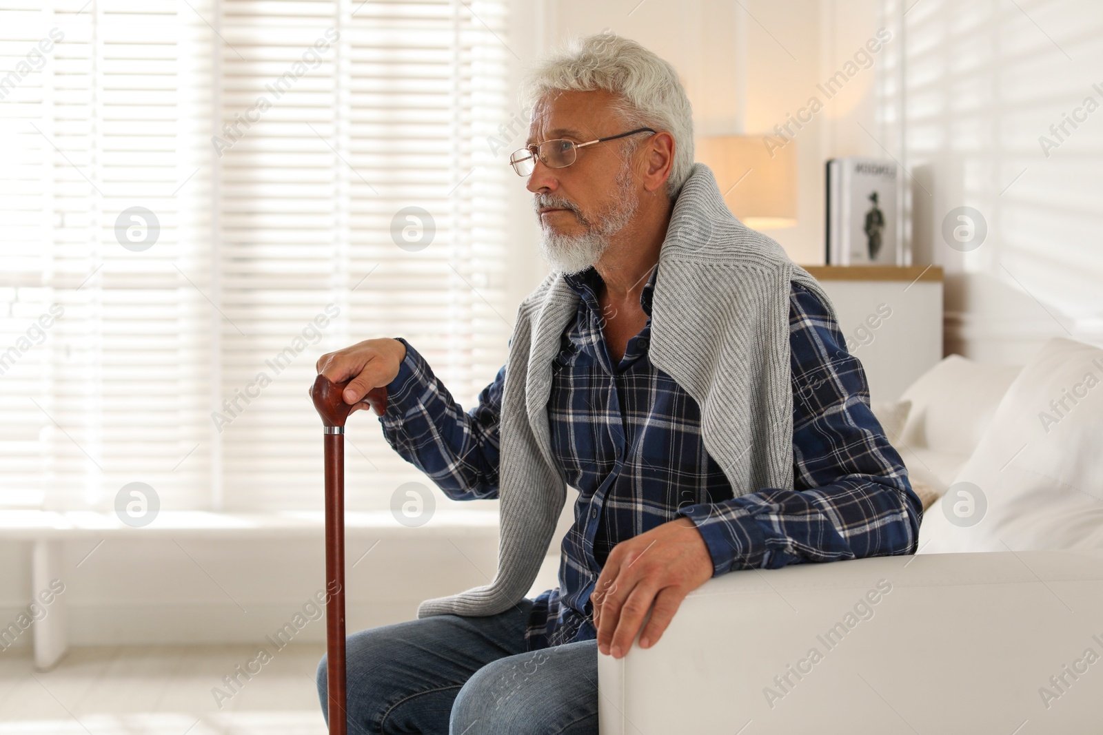 Photo of Lonely senior man with walking cane sitting on sofa at home