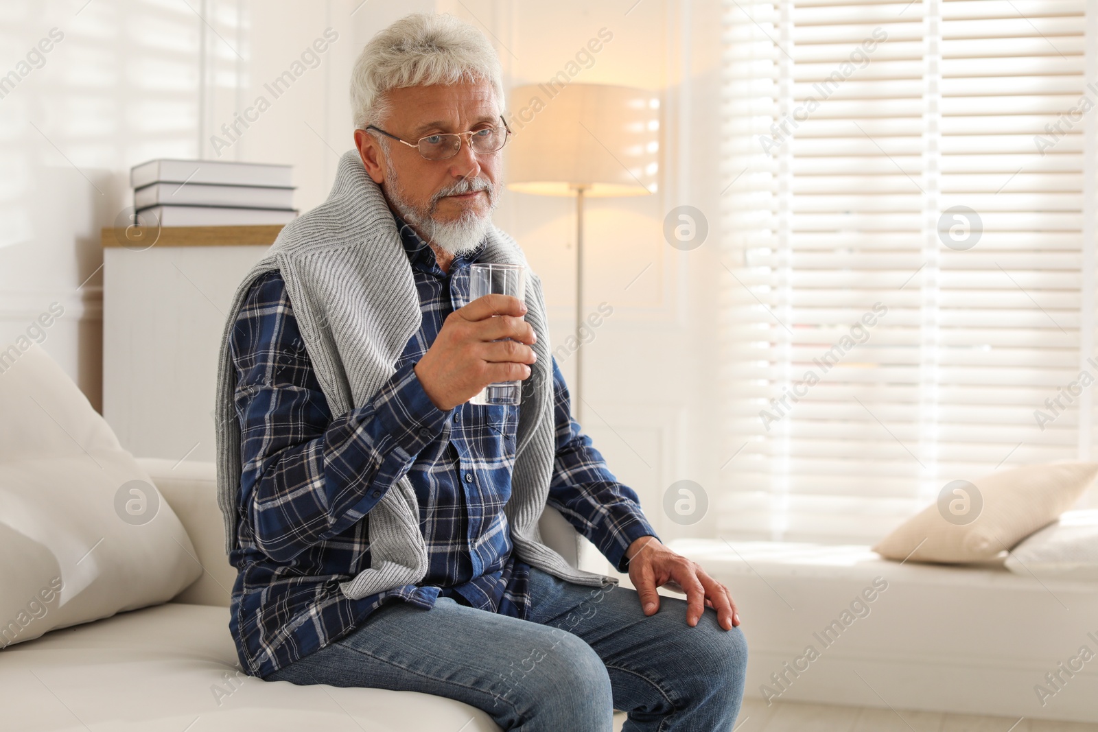 Photo of Lonely senior man with glass of water sitting on sofa at home. Space for text