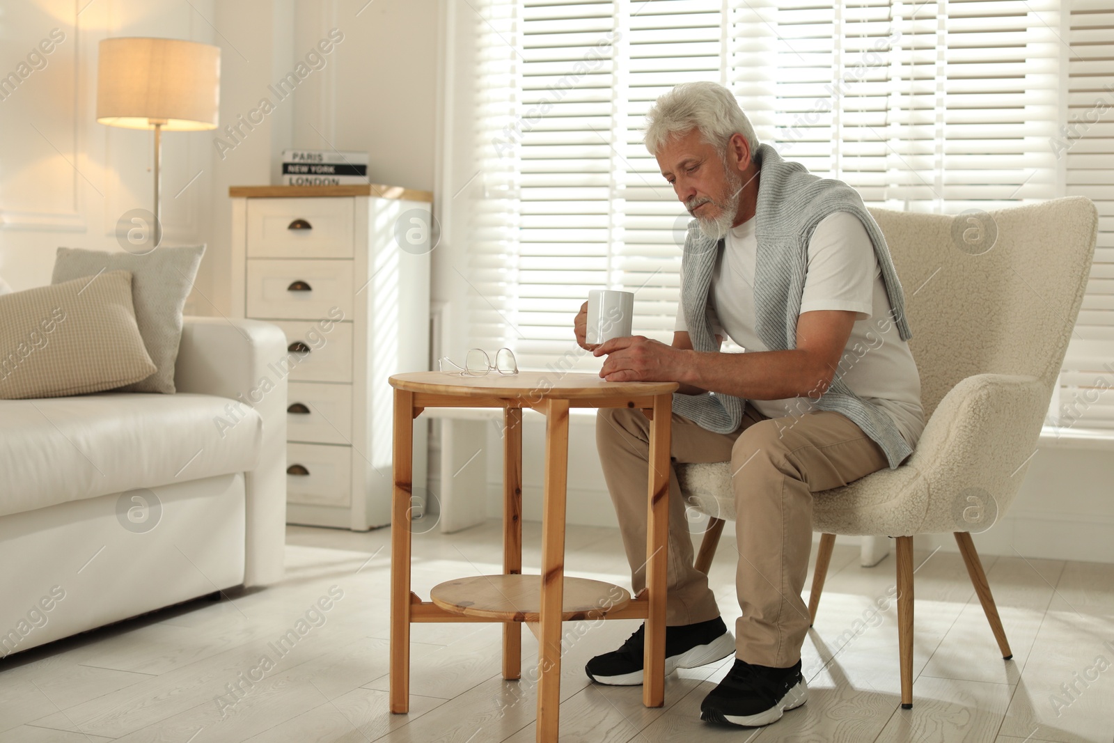 Photo of Lonely senior man with cup of drink at wooden table indoors