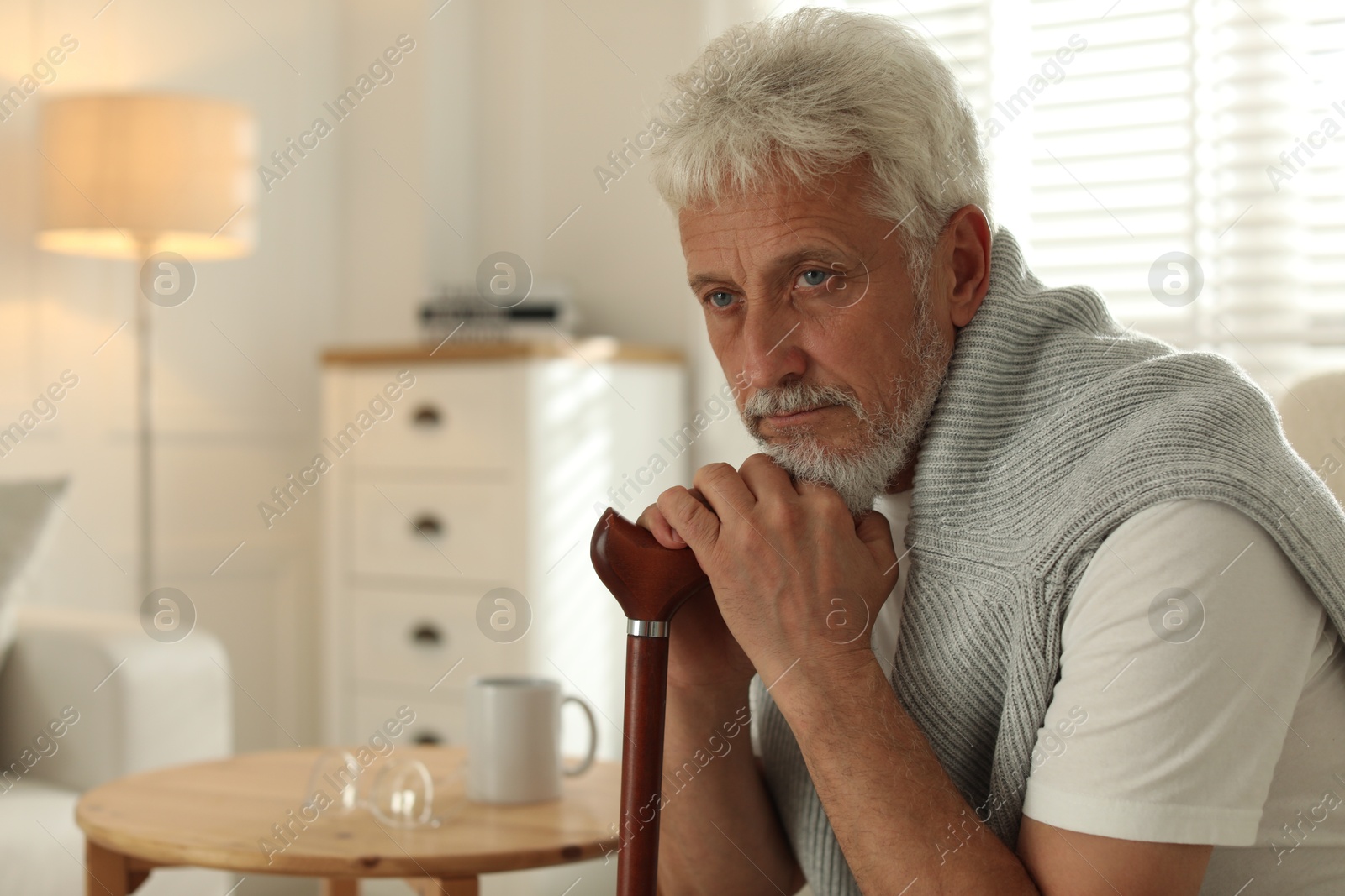 Photo of Lonely senior man with walking cane sitting in armchair at home. Space for text