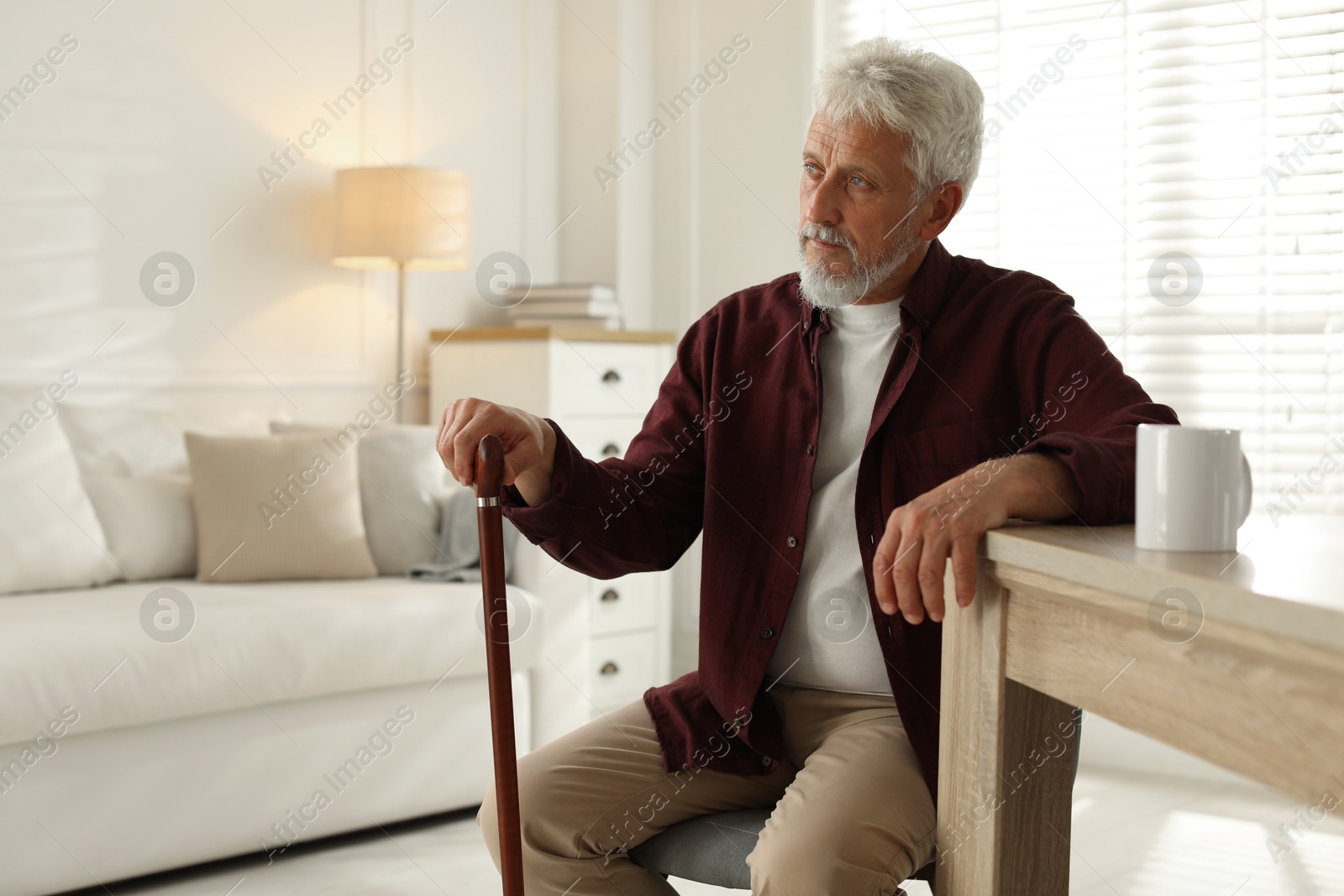 Photo of Lonely senior man with walking cane sitting at table in room