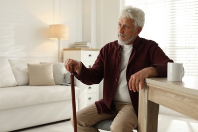 Photo of Lonely senior man with walking cane sitting at table in room