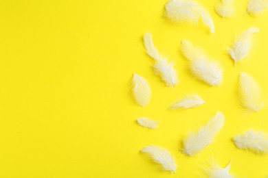 Photo of Beautiful fluffy feathers on yellow background, flat lay. Space for text