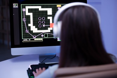 Woman in headphones playing video game with keyboard at table indoors