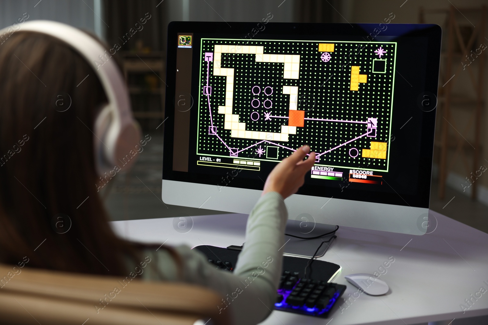 Photo of Woman in headphones playing video game with keyboard at table indoors