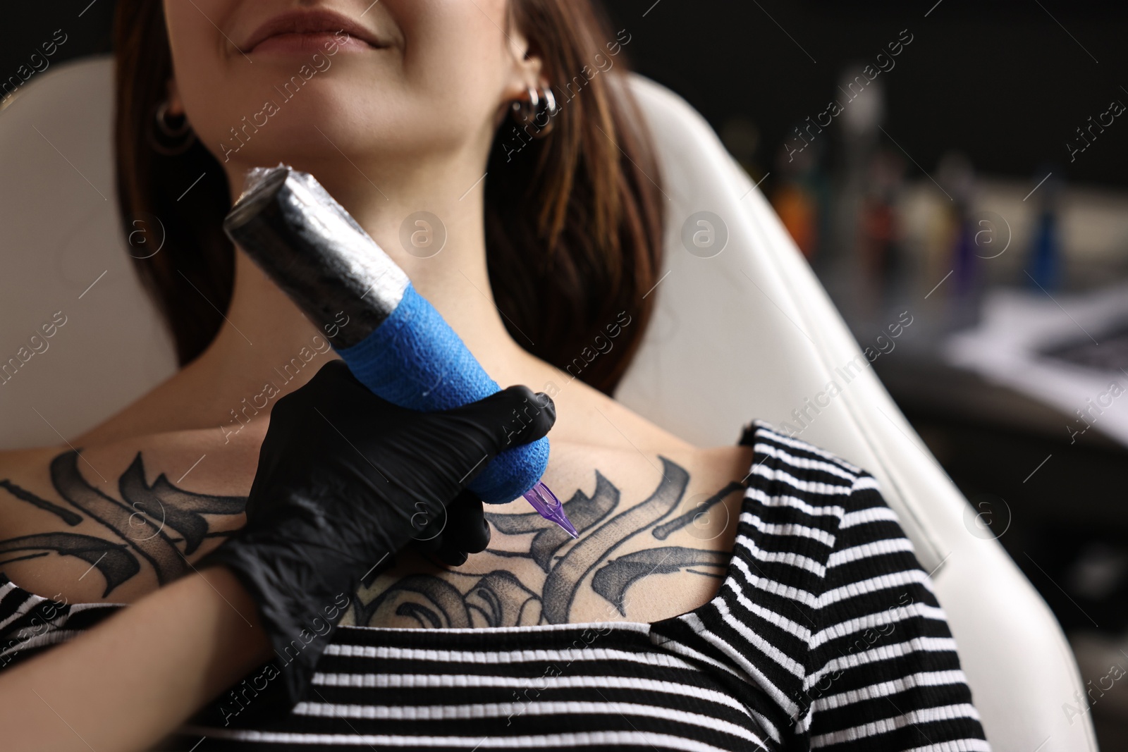 Photo of Professional artist tattooing woman with machine in salon, closeup