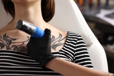 Photo of Professional artist tattooing woman with machine in salon, closeup