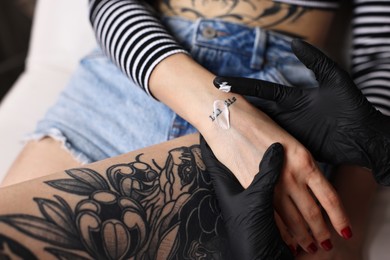 Professional artist in gloves applying cream onto woman's hand with fresh tattoo in salon, closeup