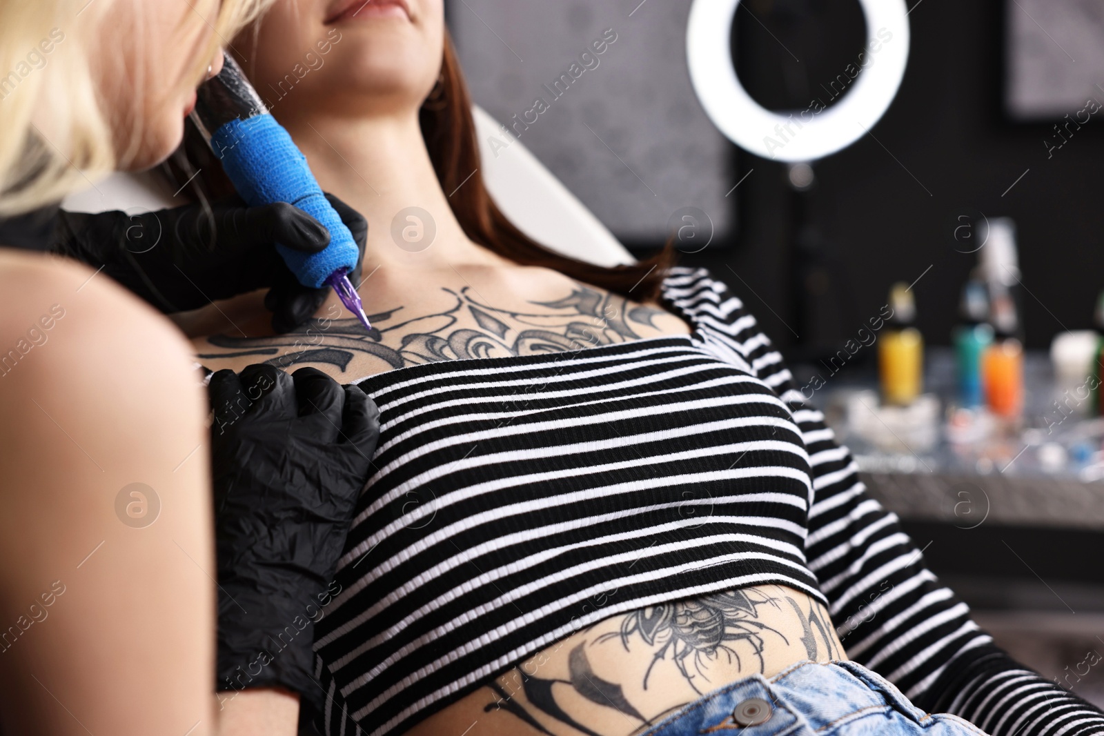 Photo of Professional artist tattooing woman with machine in salon, closeup