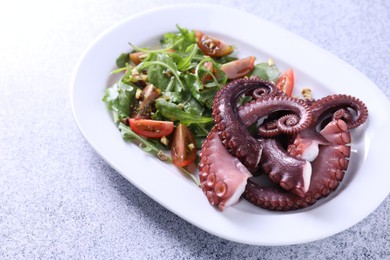 Photo of Plate with tasty boiled octopus tentacles and salad on grey textured table, closeup