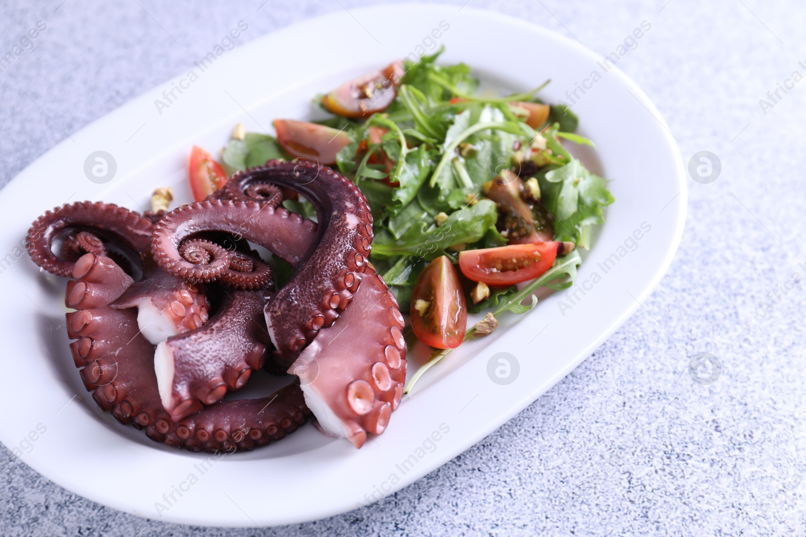 Photo of Plate with tasty boiled octopus tentacles and salad on grey textured table, closeup