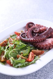 Photo of Plate with tasty boiled octopus tentacles and salad on grey textured table, closeup