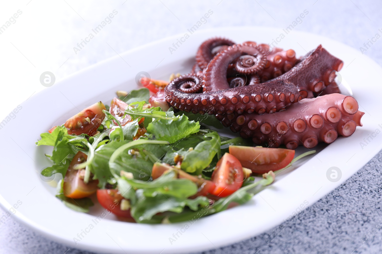 Photo of Plate with tasty boiled octopus tentacles and salad on grey textured table, closeup